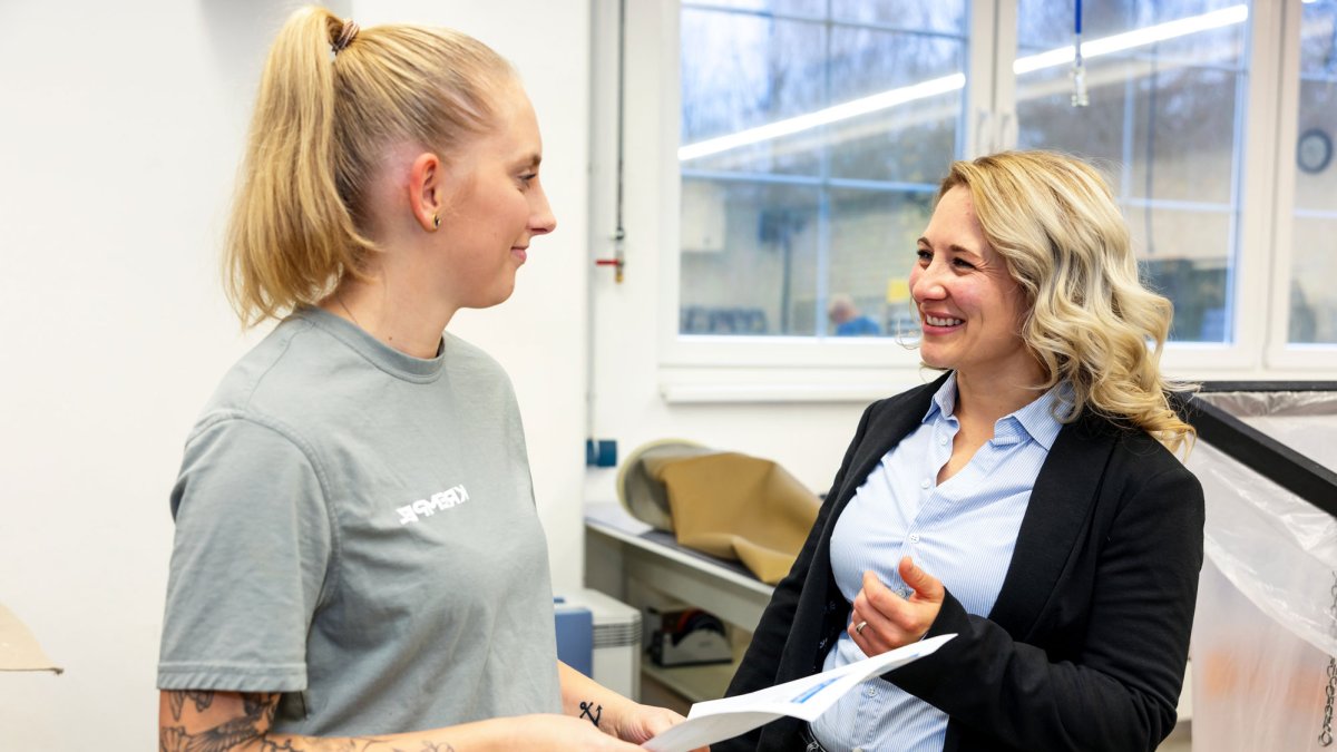 Two young woman standing in a production area looking at each other an discussing a topic