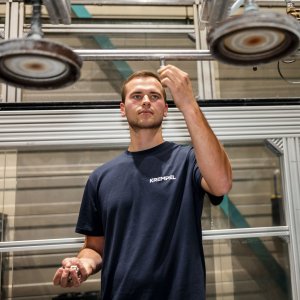 Young man is standing in a production area and working on a machine