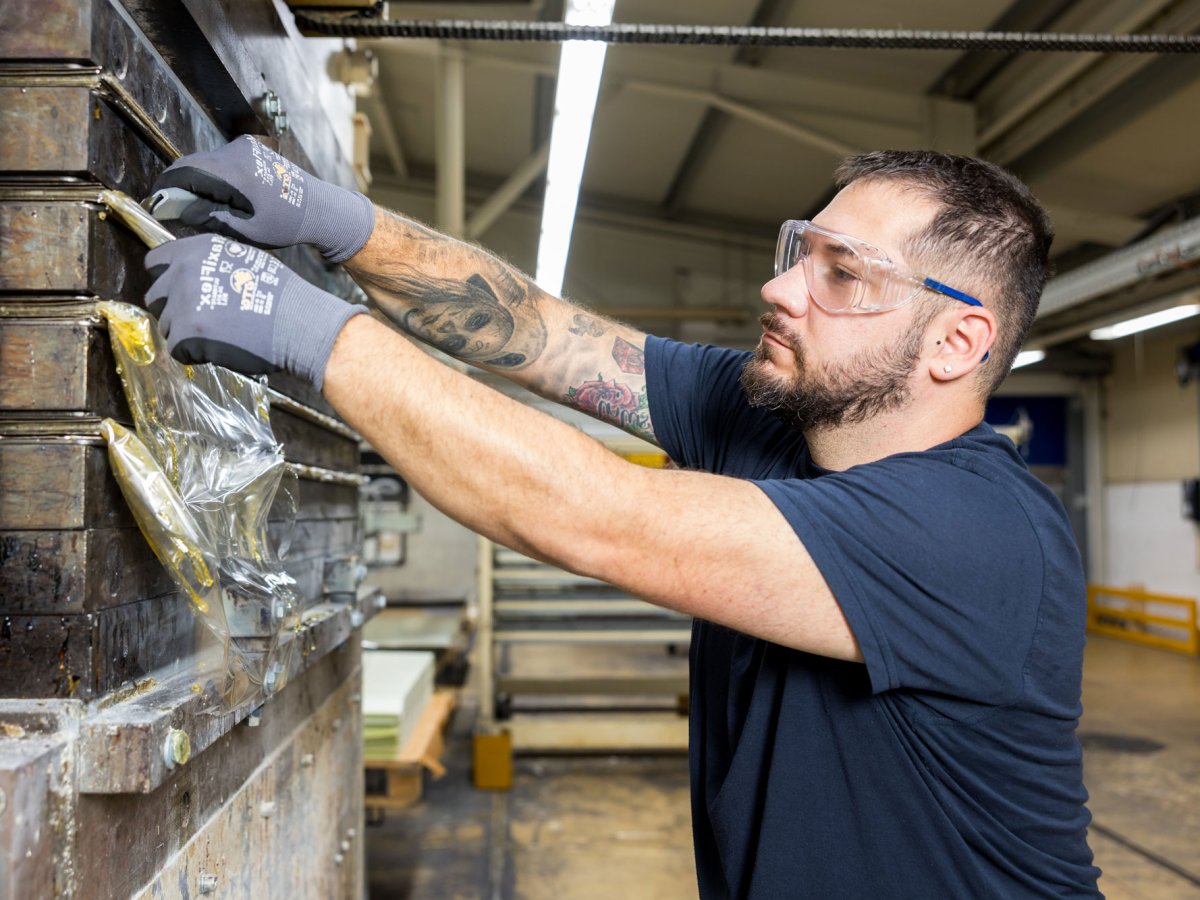 Young man working at a machine and cutting material with a pocket knife