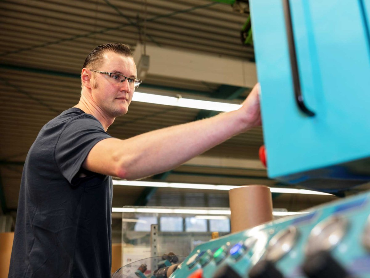Young man with glasses standing in front of a machine control panel and pressing a button