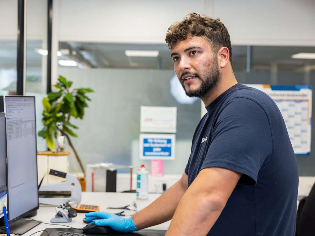 Young man is standing in front of a computer in a lab and looking at the camera